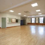The Peter Griffits Hall is another venue within the Forest Row Village Hall. Image shows the interior of the hall, taken from the entrance towards the serving hatch, which is open. At the other side of the hall can be seen the emergency exit door.